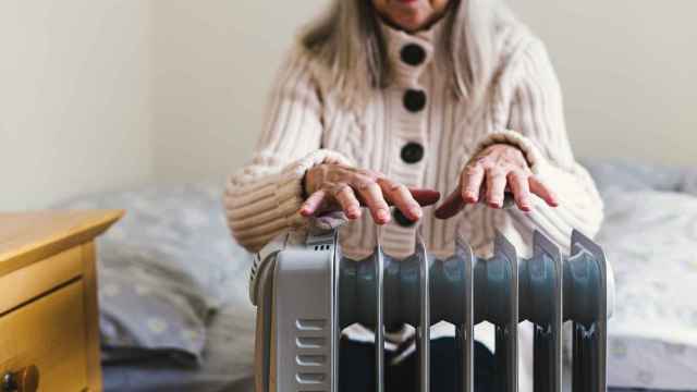 Una mujer mayor calienta sus manos en un radiador eléctrico.