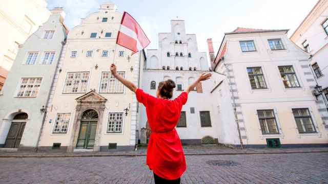 Una mujer posa con una bandera de Letonia frente a un edificio de Riga.