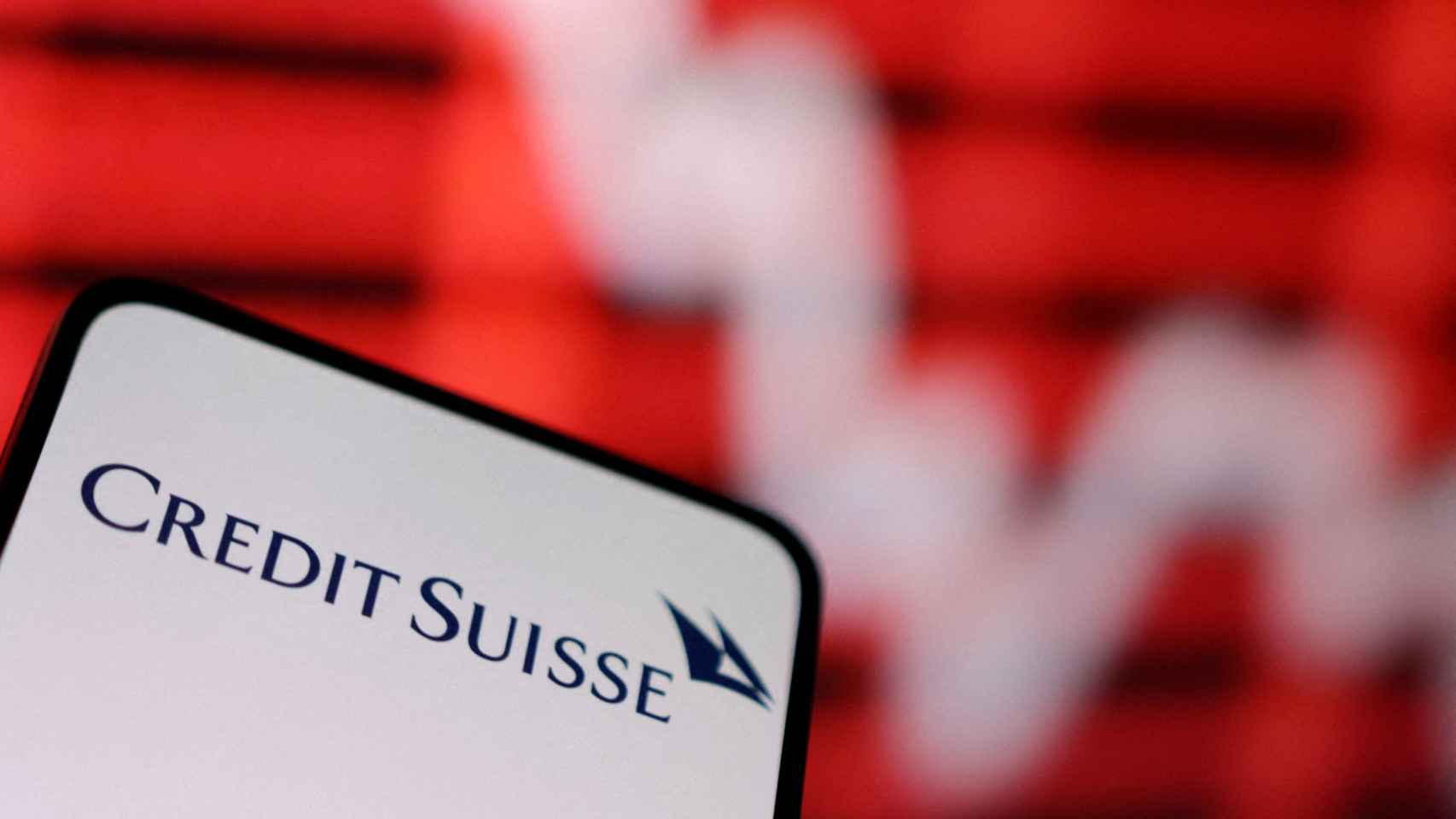 Logo de Credit Suisse en la pantalla de un teléfono móvil ante un gráfico de bolsa.