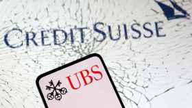 Logo de UBS en la pantalla de un móvil sobre el de Credit Suisse bajo cristales rotos.