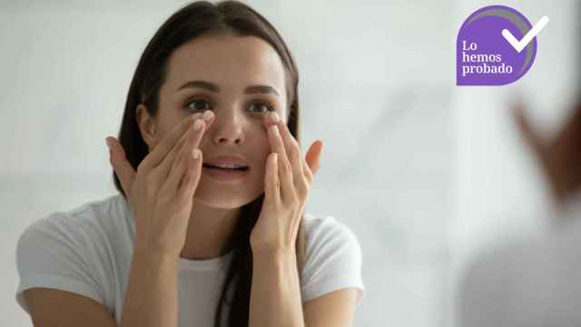 Una mujer se aplica un tratamiento de contorno de ojos ante el espejo.