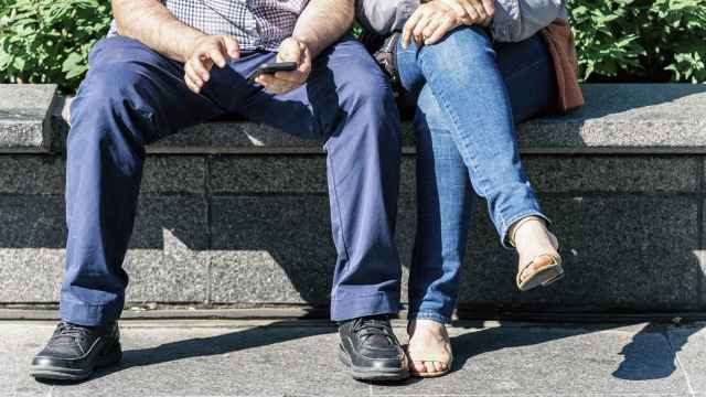 Un hombre sentado con las piernas abiertas mientras que a su lado una mujer las mantiene cruzadas.