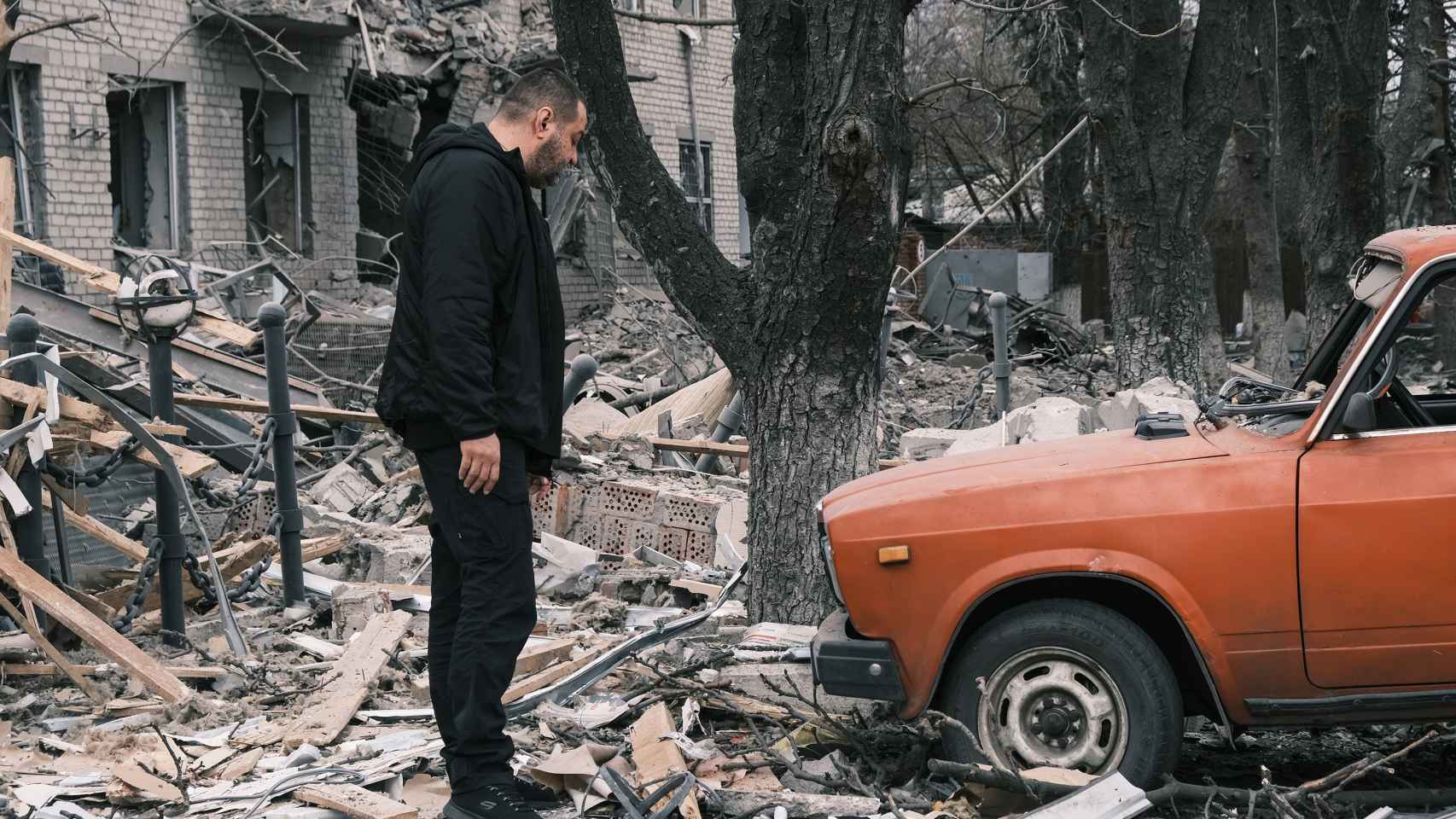 Un hombre contempla uno de los vehículos que estaban aparcados frente al edificio bombardeado en Sloviansk este lunes. Los cascotes que han caído sobre el parabrisas y el capó lo han destrozado.