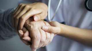 Una sanitaria sostiene la mano de un paciente.