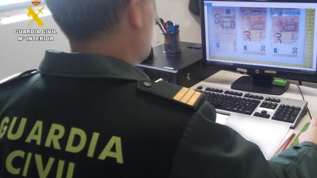 Una agente de la Guardia Civil observando una imagen de los billetes falsos