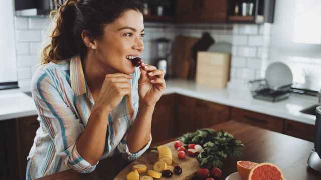 Mujer desayunando fruta en la cocina.