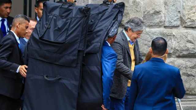 El presidente de Ecuador, Guillermo Lasso (d), sale protegido con mantas antibalas hoy, del Centro Cultural Metropolitano, en Quito (Ecuador).