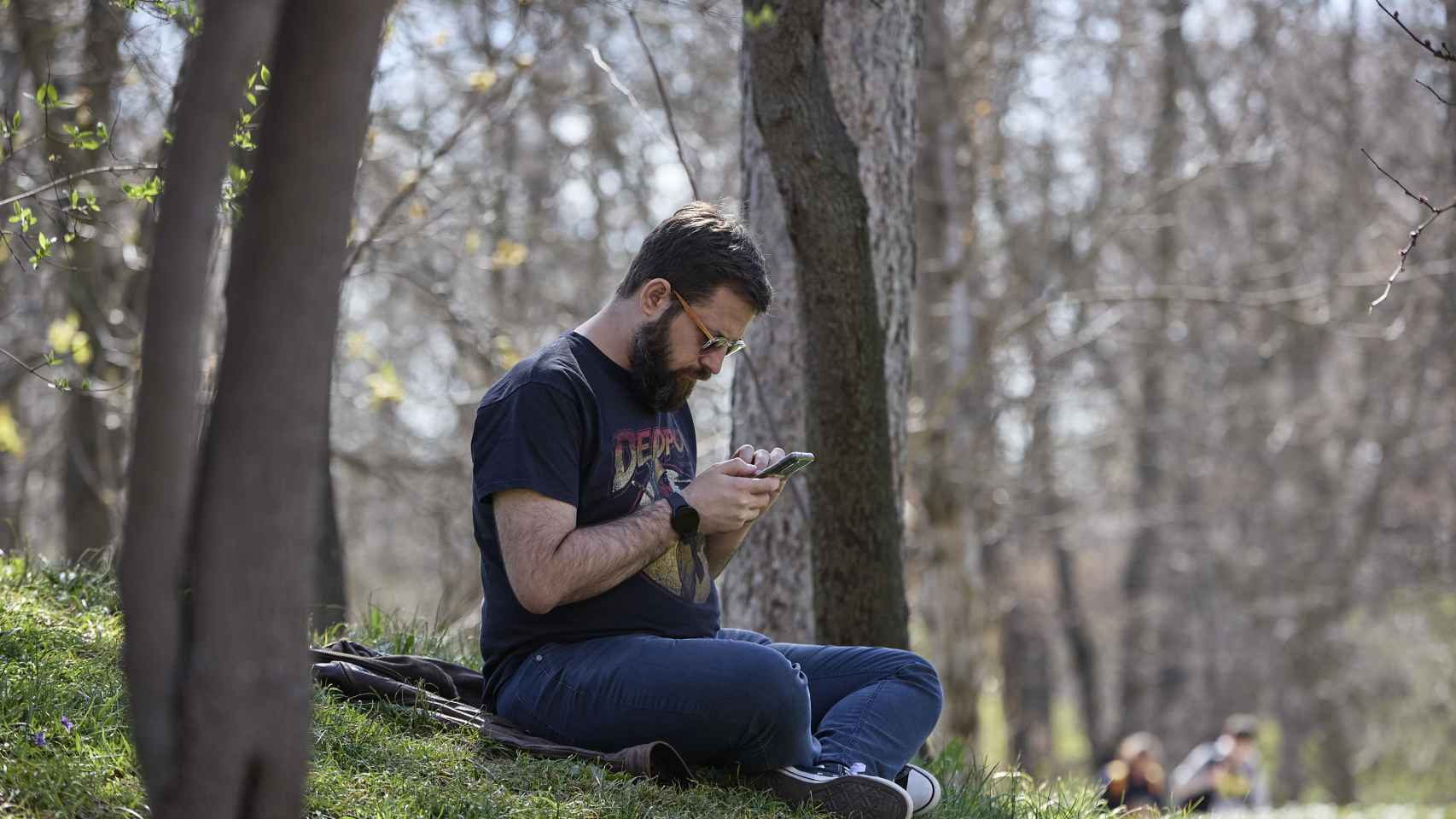 Un hombre mira su teléfono móvil en el Parque del Retiro (Madrid).