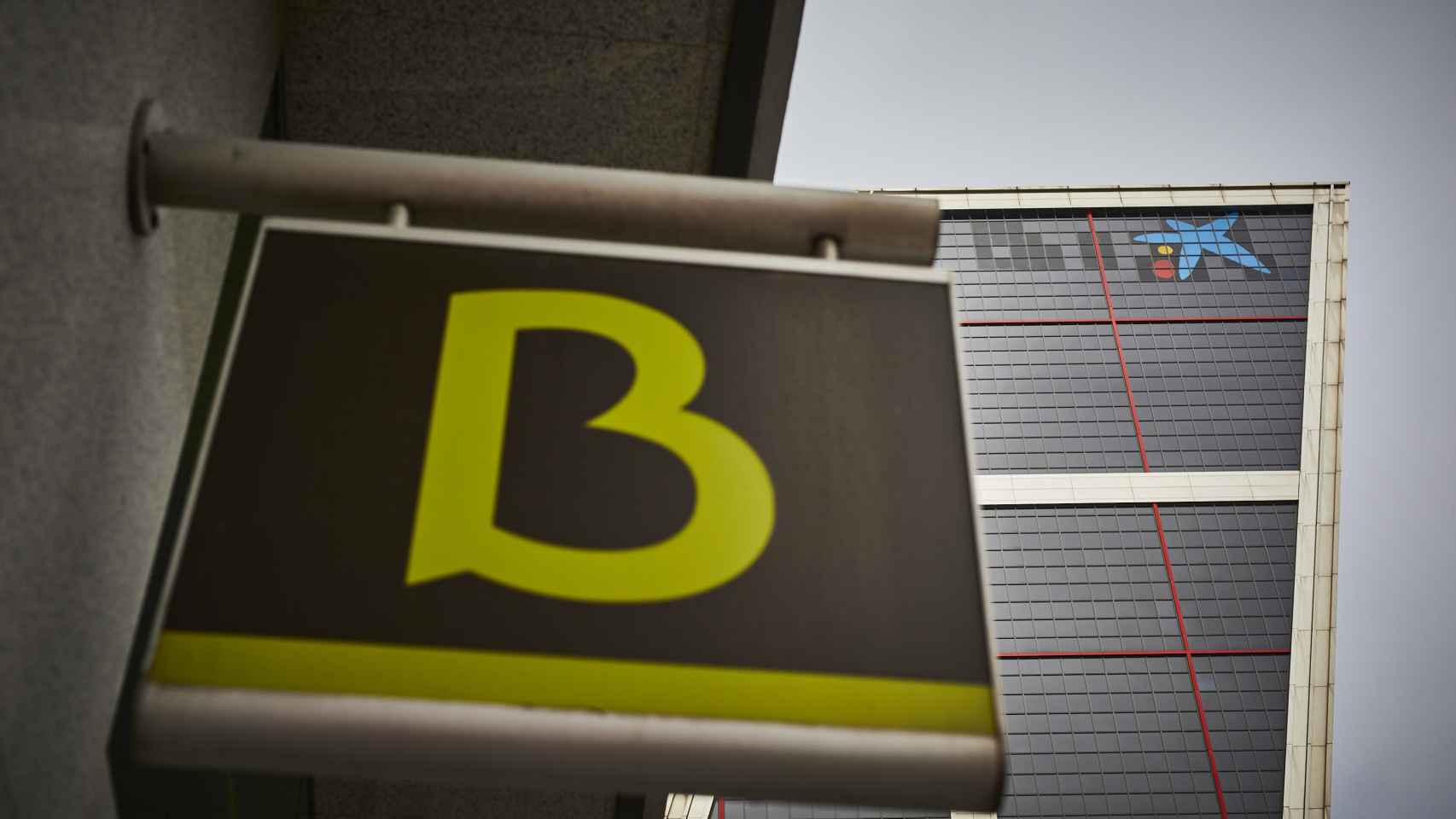 Un cartel con el símbolo de Bankia delante del logo de Caixabank tras su sustitución por el de Bankia en las torres Kio, en Madrid (España).
