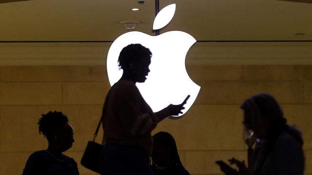 Una mujer usando su iPhone frente al letrero luminoso de la tienda de Apple en la estación Grand Central de Nueva York.