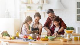 Familia cocinando juntos en la cocina rodeados de alimentos frescos.