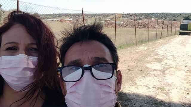 Beatriz y Jaime, posando con mascarillas, junto a la valla del aserradero que se levanta frente a su casa en el pueblo madrileño de Villamanta.