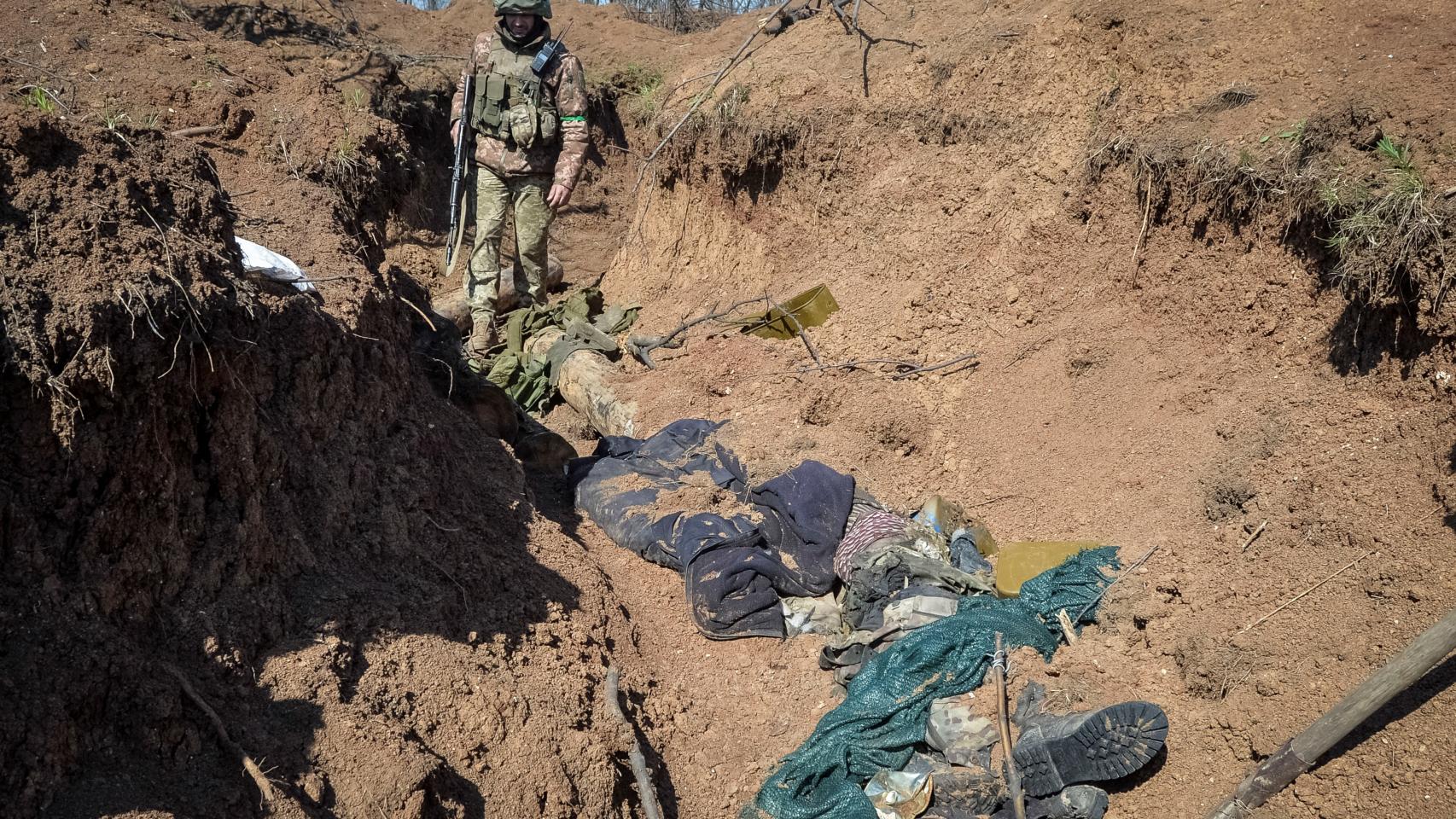 A Ukrainian military service member looks at the body of a slain Russian soldier lying in a trench at a front line position, as Russia's attack on Ukraine continues, near the town of Bakhmut, Ukraine.