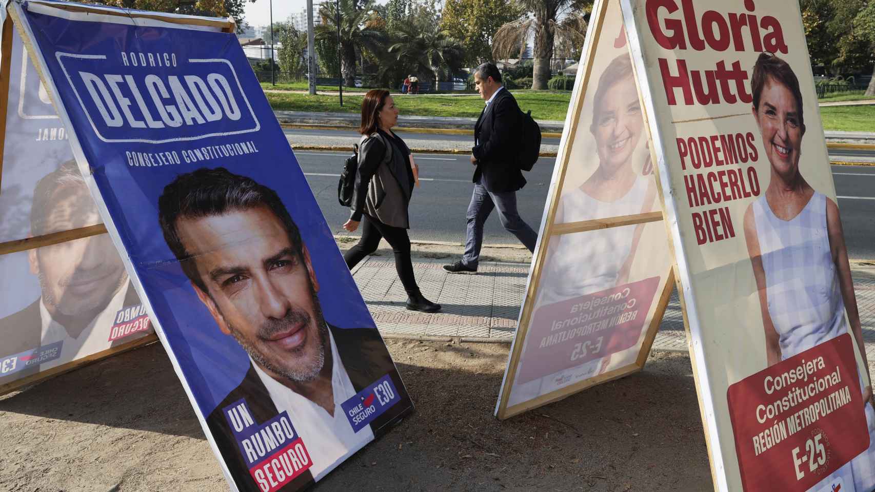 Dos personas caminan frente a carteles de propaganda electoral, el 27 de abril en Santiago.
