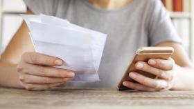 Una mujer sujetando un teléfono móvil y varias facturas.