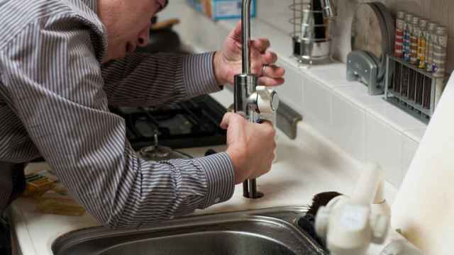 Un fontanero arregla un grifo en una vivienda en alquiler.