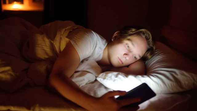 Imagen de archivo de un adolescente utilizando el móvil por la noche en una cama.