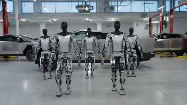 Varios robots humanoides de Tesla caminando con algunos Cybertruck  de fondo.