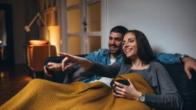 Una pareja en el sofá y con manta viendo la tele.