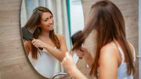 Una mujer joven se peina frente al espejo.