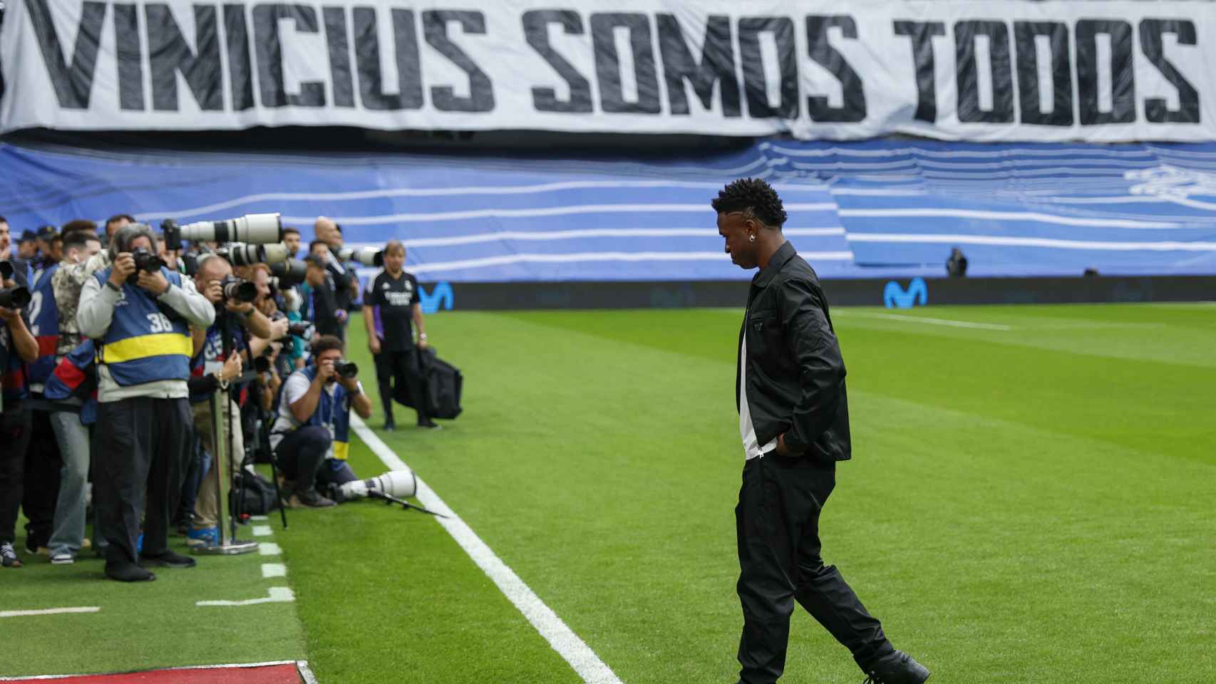 Vinicius, sobre el césped del Bernabéu con una gran pancarta al fondo.