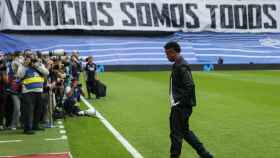 Vinicius, sobre el césped del Bernabéu con una gran pancarta al fondo.