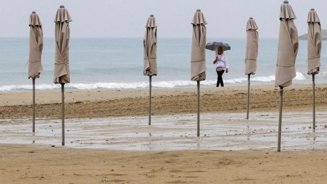 Una persona pasea bajo la lluvia por la playa de El Postiguet de Alicante.