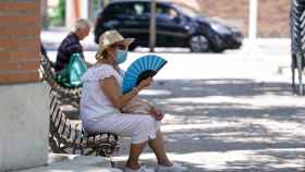 Una anciana con mascarilla se abanica sentada en un banco.