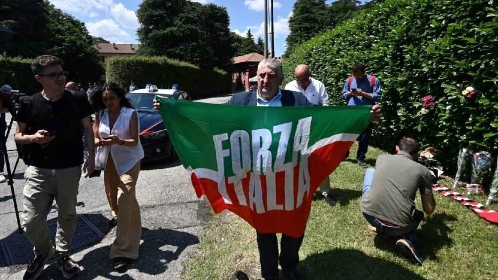 Un hombre sostiene una bandera del partido Forza Italia frente a la Villa San Martino, residencia de Silvio Berlusconi, aonde se acercó para rendirle homenaje tras su muerte, el 12 de junio de 2023 en Arcore, al norte de Italia.