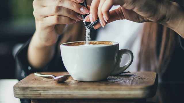 Las manos de una mujer que echa azúcar en su taza de café.