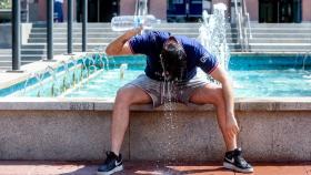 Un joven trata de refrescarse con agua de una fuente durante una ola de calor en Madrid.