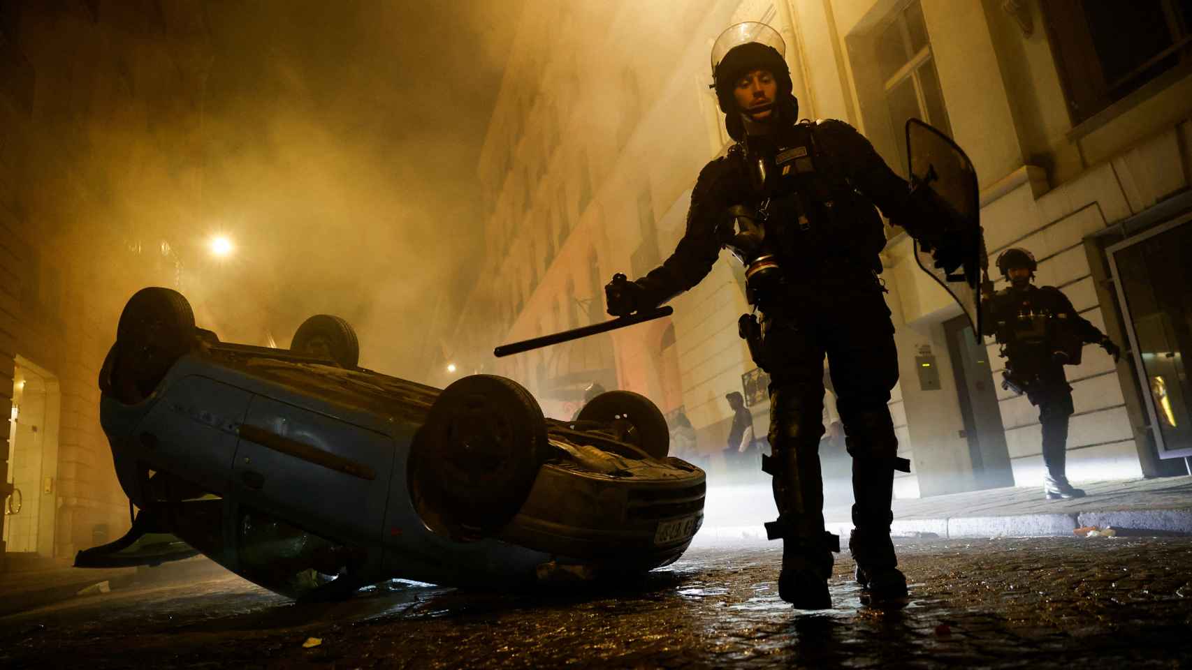 Un policía camina al lado de un coche volcado en París durante los disturbios.
