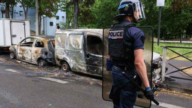 Un antidisturbios francés frente a vehículos calcinados por los disturbios