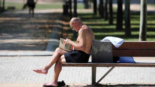 Un hombre sin camiseta lee un libro en un parque.