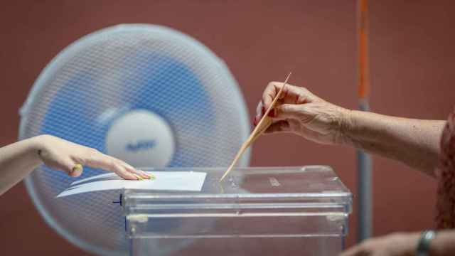 Una persona introduce su voto en la urna electoral junto a ventilador