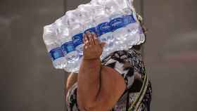Una mujer lleva botellas de agua en la playa de la Malagueta.