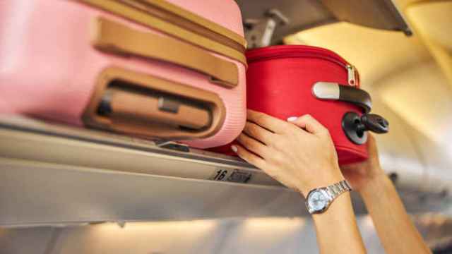 Una mujer deja su equipaje de mano justo encima de su asiento en un avión