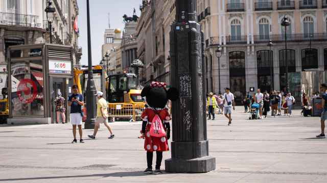 Una mujer disfrazada de Minnie busca resguardo a la sombra de una farola en la Puerta del Sol.