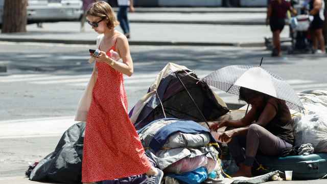 Una mujer en situación de sinhogarismo se protege del sol bajo una sombrilla.