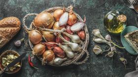 Cesta con cebollas, cebolletas y ajos sobre una mesa. Foto: Getty Images.