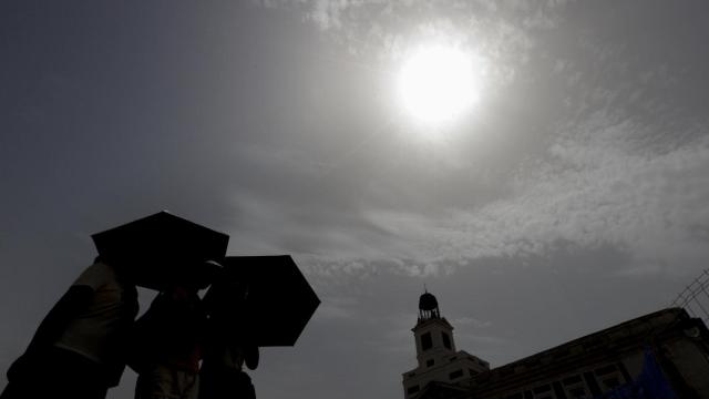 Varios viandantes se protegen del sol mientras cruzan la Puerta del Sol de Madrid.