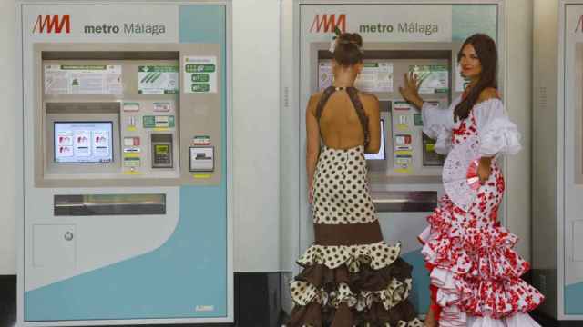 Dos mujeres vestidas de gitana compran billetes para el Metro de Málaga.