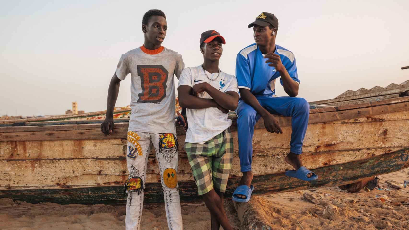 De izquierda a derecha, Ignace, Mohamed y Jibril charlan apoyados sobre el cayuco pesquero con el que salen a faenar al Atlántico.