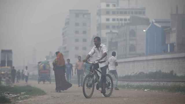 Imagen de archivo de un hombre que monta en bicicleta entre el humo que sale de las acerías situadas cerca de un barrio marginal de Dhaka.