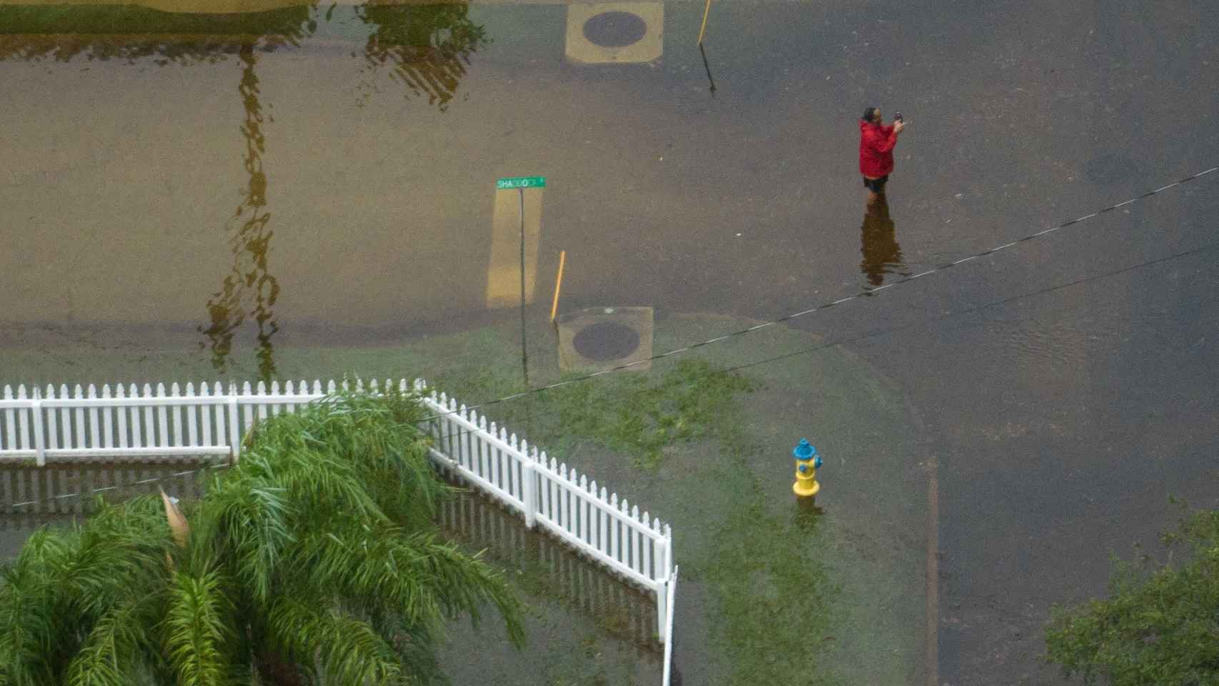 Una mujer sacando fotos en medio de una calle inundada en Tarpon Springs.