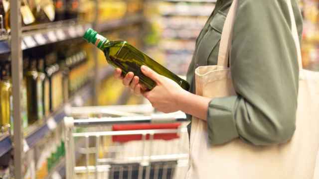 Una mujer elige una botella de aceite en el supermercado.