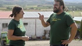 Dos de los miembros de la asociación Guzmán Renovable, Beatriz García y Diego Cabrito, y al fondo la nave en cuya cubierta están instalando placas solares
