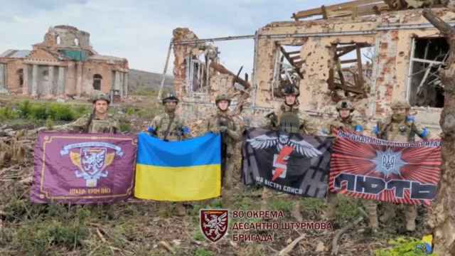 Los soldados sostienen banderas mientras hablan frente a edificios destruidos en Klishchiivka, Ucrania.