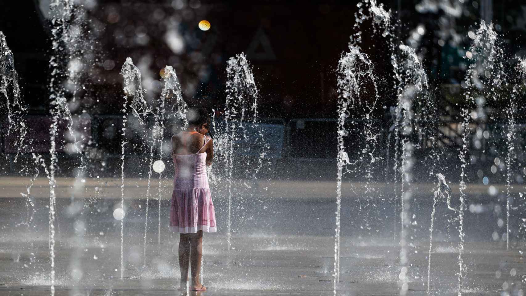 Una niña juega en una fuente para refrescarse del calor.