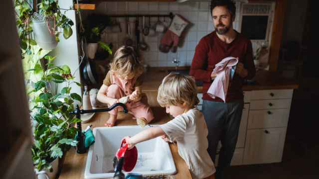 Un padre juntos a sus dos hijos realizando tareas domésticas.
